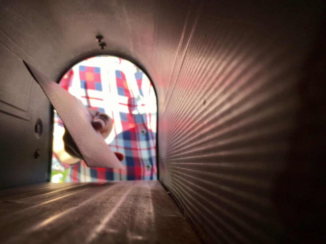 Looking Through a mailbox to see Woman’s hand taking or placing letter in mailbox