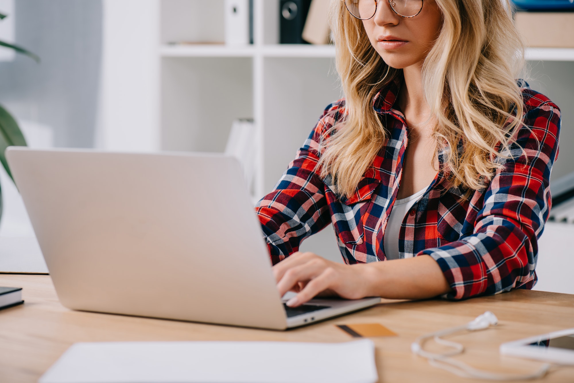 partial view of woman typing on laptop at tabletop with credit card and papers